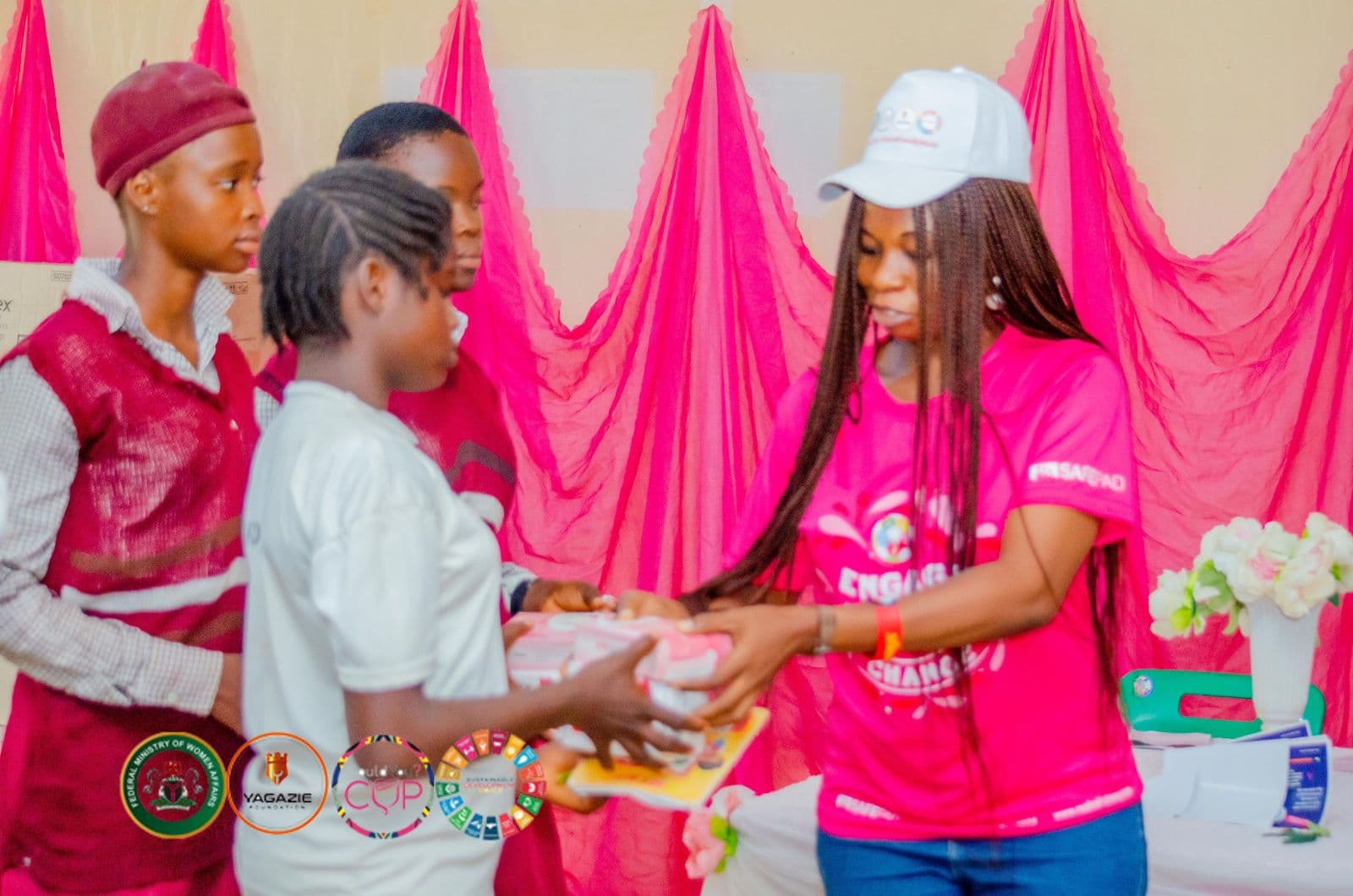 A volunteer in a pink shirt hands a pack of products to a student
