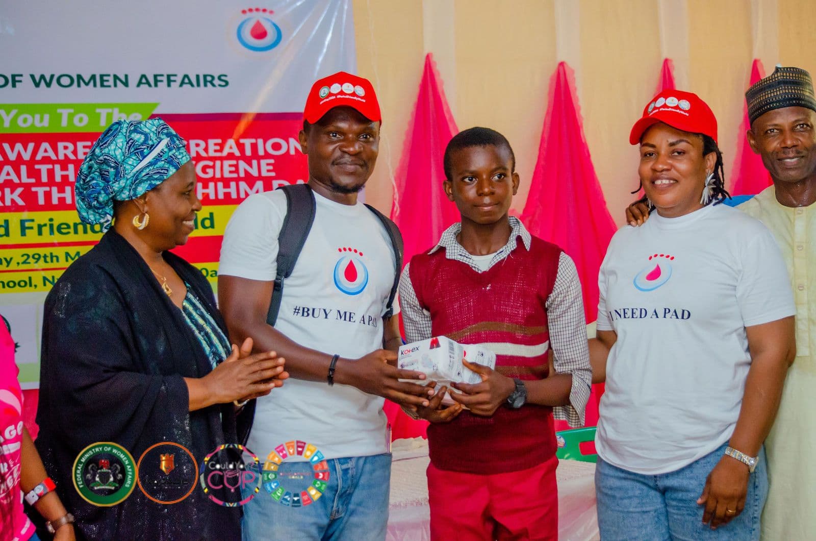 Volunteers and a student pose with menstrual products beside the campaign banner