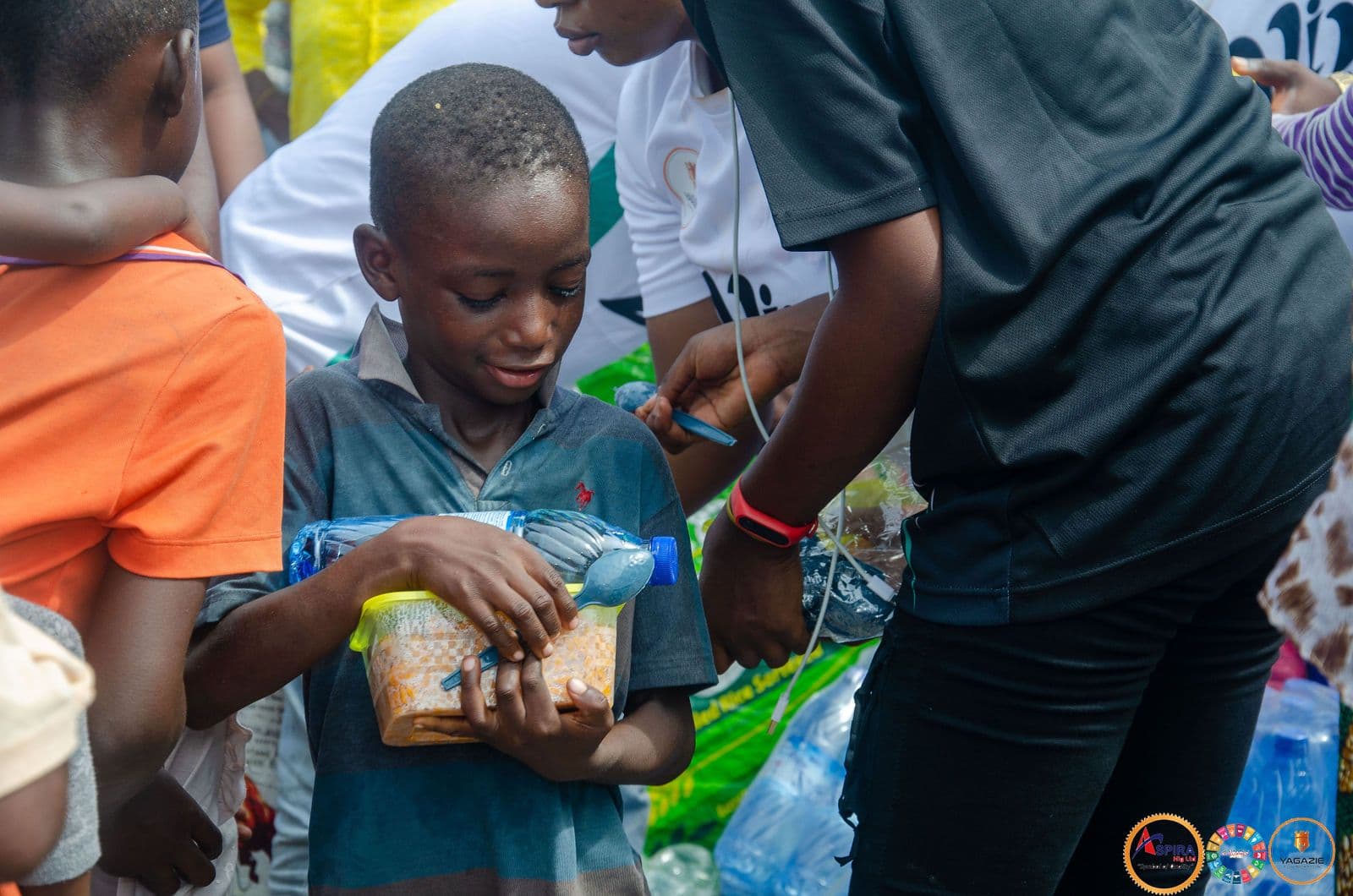 A boy receives a food pack and water from a volunteer